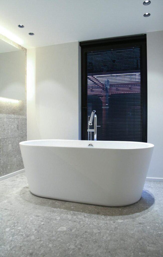 An image of a white bathtub with a black window in the background and gray walls and flooring.